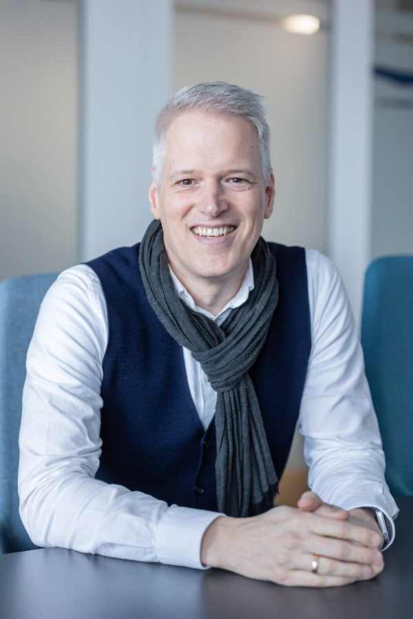 Christian Buß sitzt an einem Tisch und lächelt in die Kamera