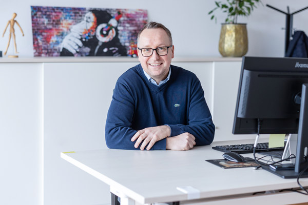 Marc Ellinghaus sitzt an einem weißen Tisch und lächelt in die Kamera