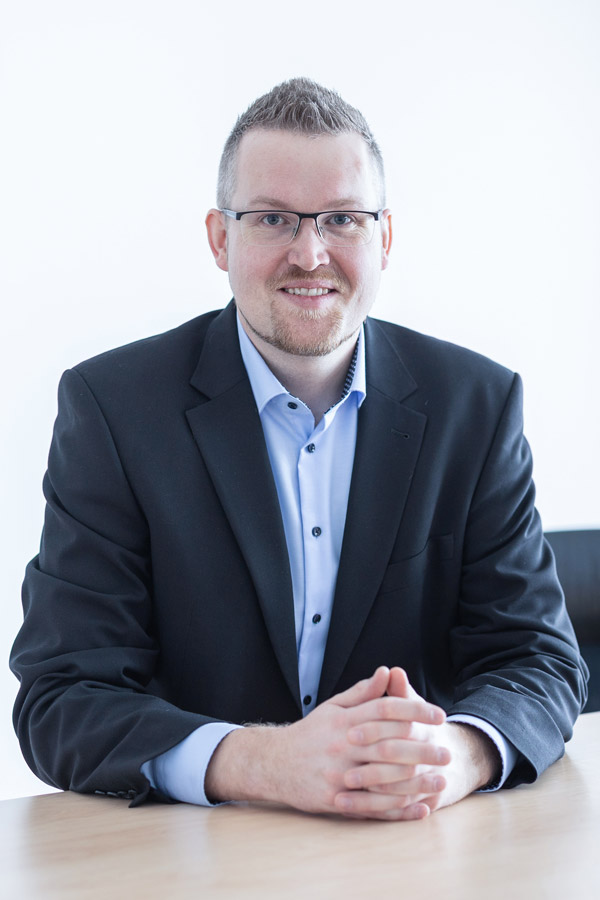 Jörn Hillmer sitzt an einem Tisch und lächelt in die Kamera