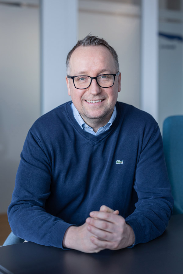 Marc Ellinghaus sitzt an einem Tisch und lächelt in die Kamera