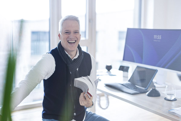 Christian Buß sitzt lachend in seinem Büro