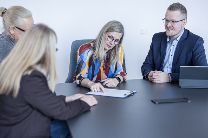 Nicole Buß und Jörn Hillmer sitzen mit zwei Mandanten am Tisch und erklären etwas auf einem Dokument